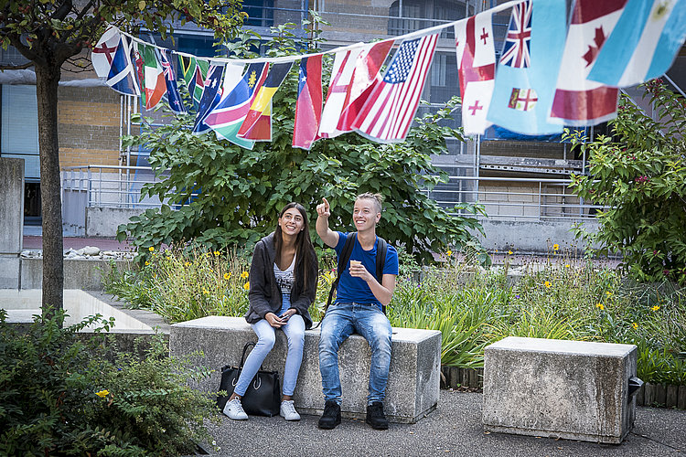 Deux étudiants dans un bâtiment de l'université Lyon 3, devant des drapeaux de plusieurs pays.